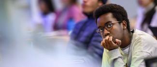 A student wearing glasses is sitting in a classroom while looking focused.