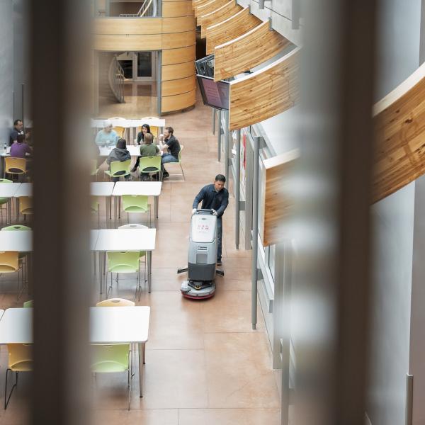 A man is moving an industrial floor scrubber across the floor in the atrium of the Michael Smith Labs.